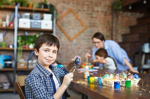 Portrait of smiling boy  while painting eggs for Easter in art studio, copy space