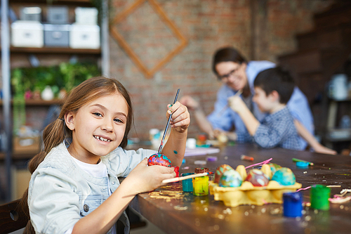 Portrait of smiling girl  while painting eggs for Easter in art studio, copy space