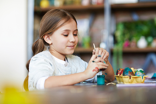 Portrait of cute girl painting eggs for easter in art studio, copy space