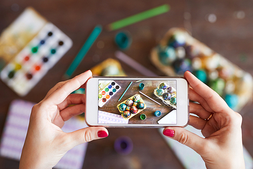 Top view closeup of unrecognizable woman taking photo of handmade Easter eggs with mobile phone, copy space