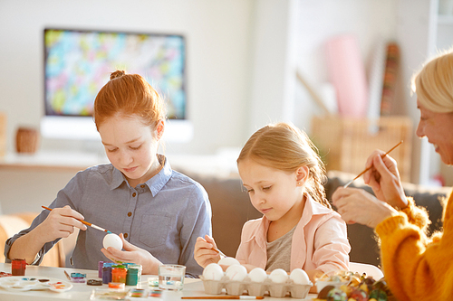 Portrait of two girls painting eggs for Easter in sunlight, copy space