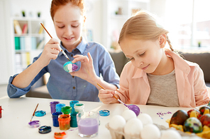 Portrait of two happy girls panting eggs for Easter in art class, lit by sunlight