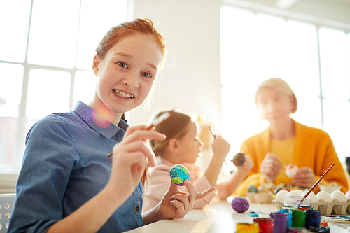 Portrait of smiling red haired girl  while painting eggs for Easter, copy space