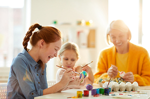 Side view portrait of excited red haired girl smiling happily while painting Easter eggs in art class, copy space