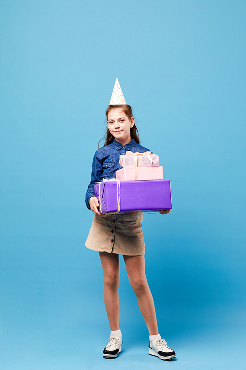 Full length portrait of teenage girl holding Birthday presents posing against pastel blue background, party concept