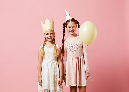 Portrait of two girls wearing party hats posing against pink background, copy space