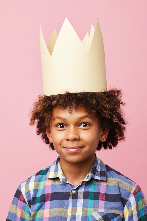 Head and shoulders  portrait of smiling African-American boy wearing crown posing against pink background, Birthday party concept