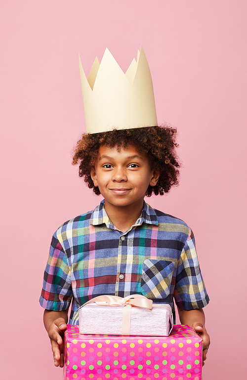 Waist up portrait of smiling African-American boy holding presents posing against pink background, Birthday party concept