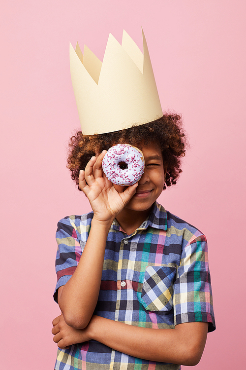 Waist up portrait of smiling African-American boy holding donut posing against pink background, Birthday party concept