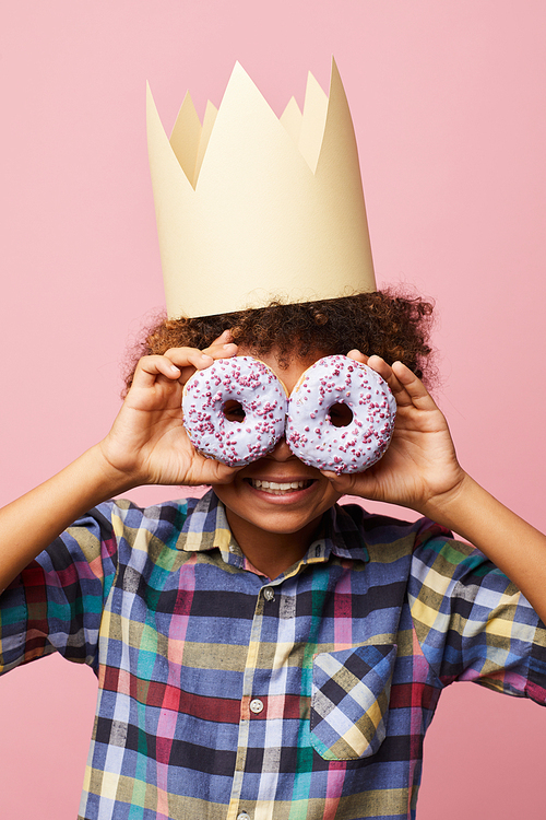 Waist up portrait of smiling African-American boy holding donuts posing against pink background, Birthday party concept
