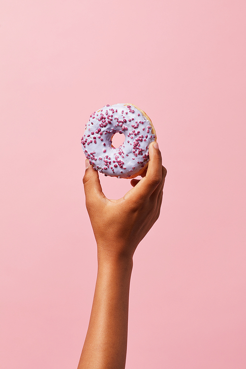 Closeup of unrecognizable African-American kid holding single glazed donut against pink background, copy space