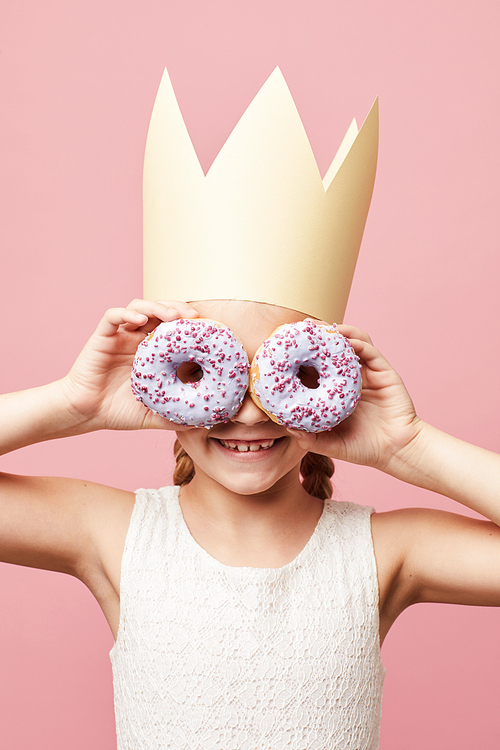 Waist up portrait of smiling girl holding donuts posing against pink background, Birthday party concept