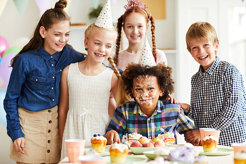 Multi-ethnic group of children celebrating Birthday standing at table together with African-American boy with face in cake