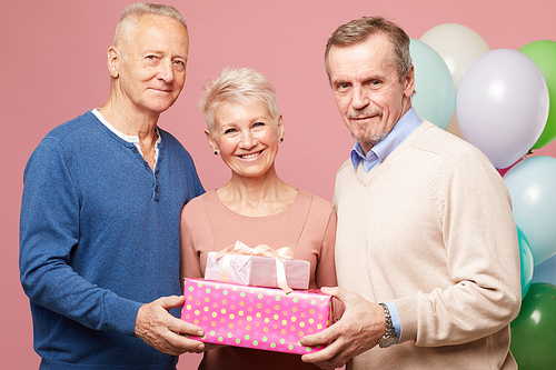Group of positive mature friends in casual outfits holding stack of gifts together and , they having fun at birthday party