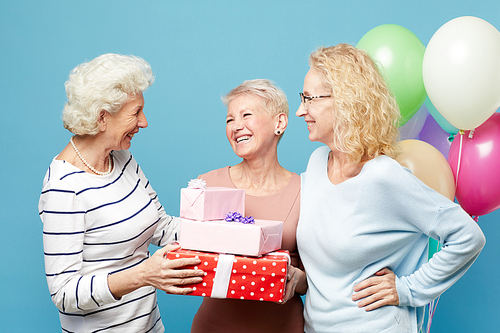 Group of cheerful lady friends congratulating birthday woman and giving stack of gift boxes to her at party