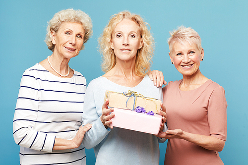 Portrait of smiling beautiful mature lady standing with best friends against blue background and holding gift boxes