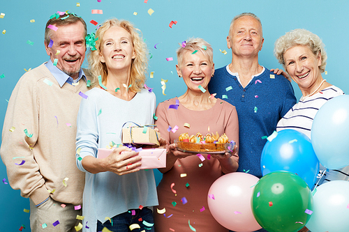 Group of happy excited mature friends in casual outfit crying from joy at birthday party while confetti falling