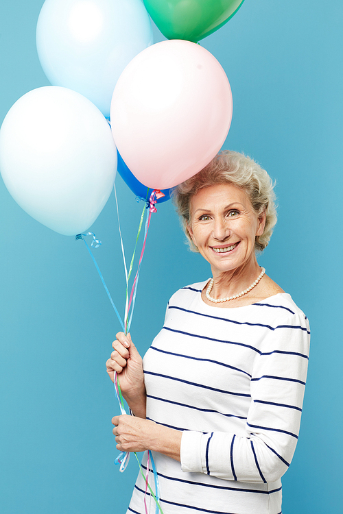 Portrait of playful pretty mature woman in stripped sweater holding heap of colorful balloons