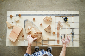 High angle view of unrecognizable carpenter standing at table and preparing slices of wood for work, desk with tools and wooden details