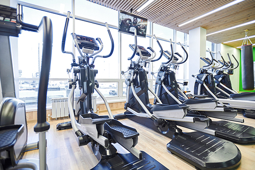 Image of modern ellipticals standing in a row against the big window in sport gym