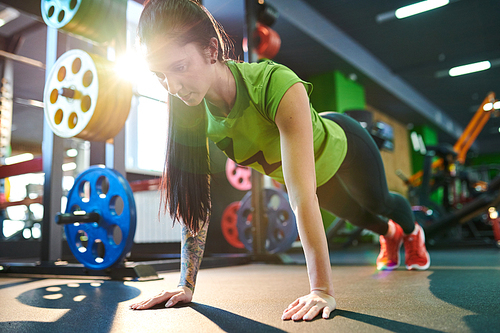 Young woman in sportswear doing push-ups before training in fitness club