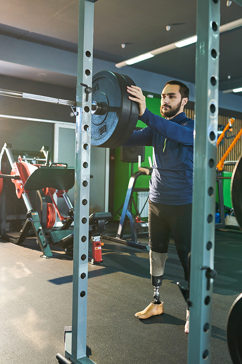 Young sportsman with amputee leg is going to training with barbell in gym