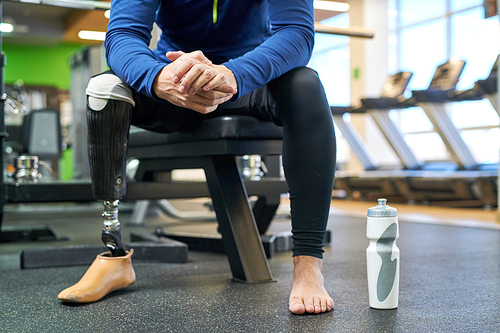 Close-up of man with amputee leg in sports clothing sitting and drinking water in gym