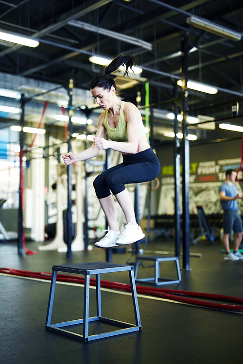 Young active woman in sportswear training on jump chair while working out in gym or fitness center