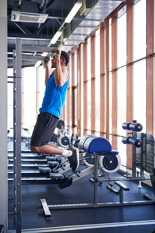 Young African-american sportsman hanging on sports bar while exercising in fitness center