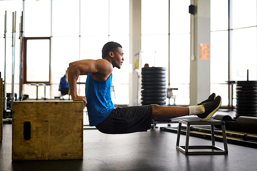 Young active African-american athlete exercising on cross training equipment in fitness center or gym