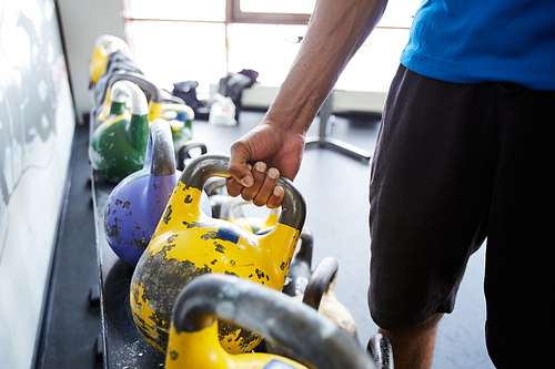 Muscular hand of young athlete in activewear taking heavy kettlebell before workout in gym