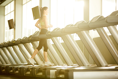 Young sportswoman in activewear practicing running on one of treadmills in fitness center or gym