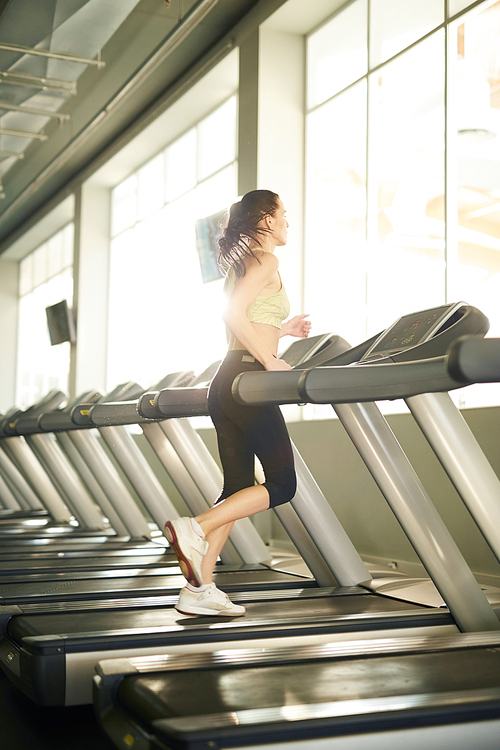 Young active brunette woman in sportswear running on one of treadmills in modern leisure center