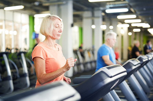 Mature blonde woman in activewear exercising on one of treadmills in contemporary sports center or gym