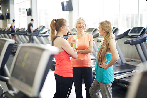 Friendly mature women in activewear dicussing something while enjoying break between trainings in fitness center