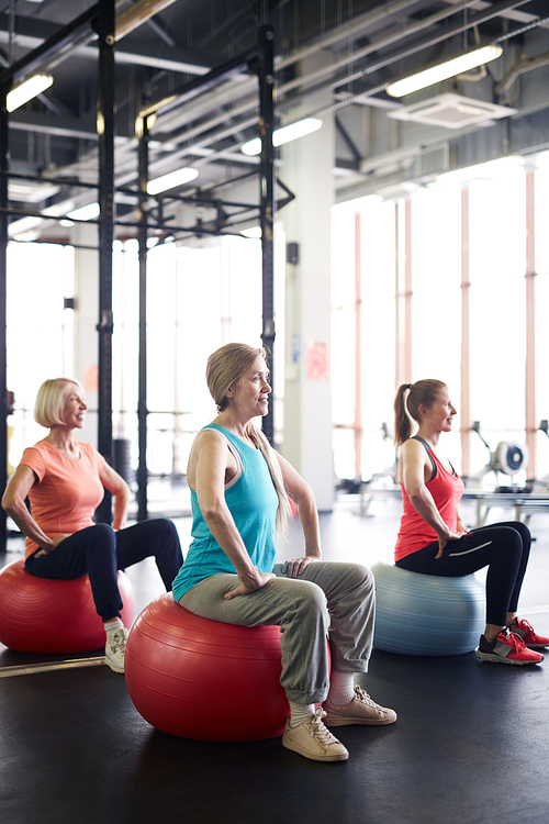 Mature sportswomen in activewear sitting on fitness balls during workout in gym or leisure center