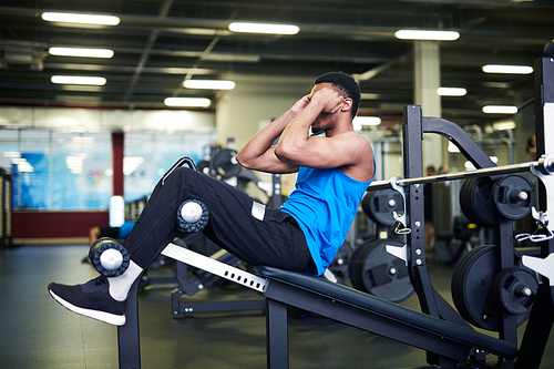 Young active man in sportswear doing sit-ups on fitness equipment in large gym or leisure center