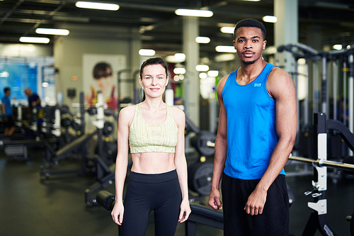 Two young active professionals in sportswear looking at you in contemporary fitness center