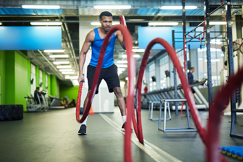 Young athlete in sportswear exercising with ropes while holding their ends during workout in gym