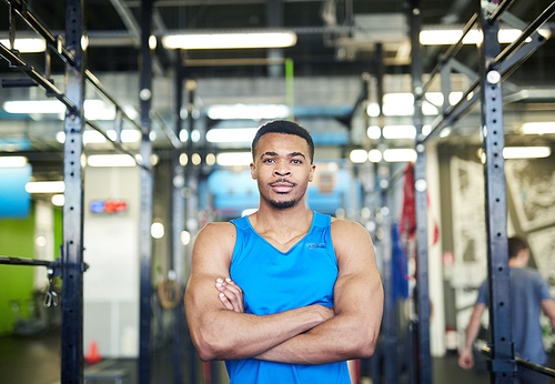 Young muscular athlete or sports coach with arms crossed on chest standing in gym in front of camera