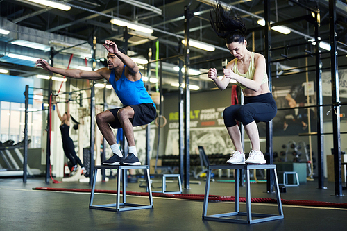 Two young active athletes in sportswear exercising on jump chairs during cross training in gym or fitness center