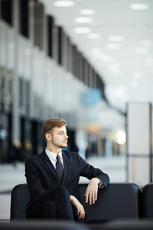 Side view portrait of young businessman relaxing in VIP lounge of airport waiting room, copy space