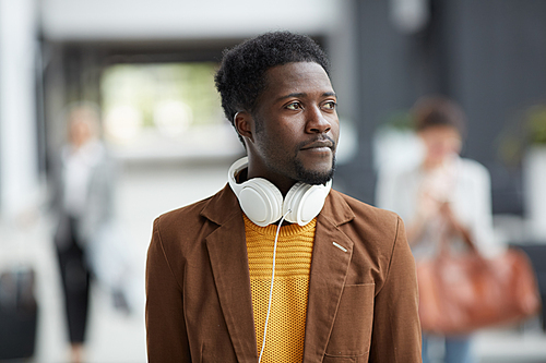 Pensive inspired young Afro-American man with white headphones on neck walking over airport and looking around