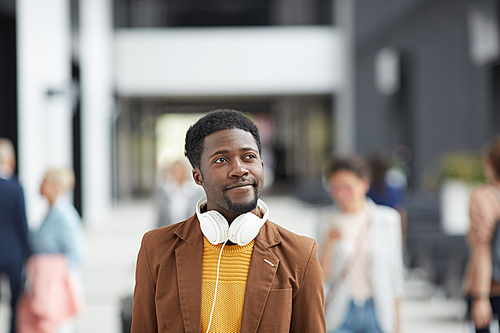 Content dreamy modern Afro-American guy with headphones crossing crowded lobby and planning vacation