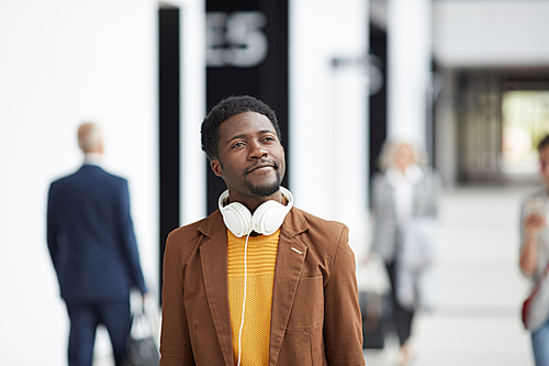 Smiling carefree Afro-American guy with wired headphones on neck walking over airport and enjoying first day of vacation