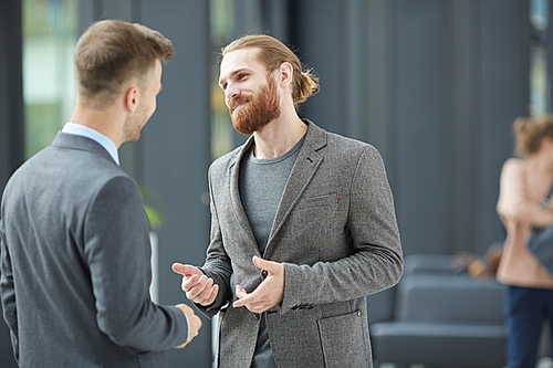 Content handsome bearded manager in jacket gesturing hands while talking to business partner