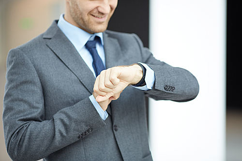 Close-up of smiling businessman in gray suit standing in lobby and checking time on wristwatch
