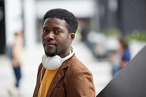 Portrait of serious handsome young black man with wired headphones on neck standing in lobby