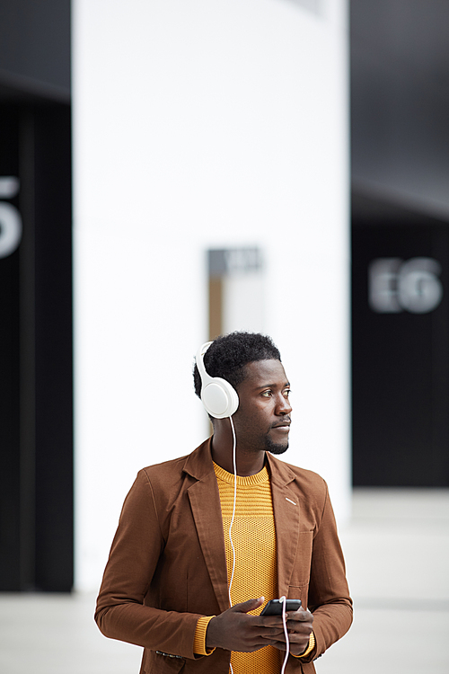 Pensive handsome young Afro-American man using smartphone app while listening to music in headphones