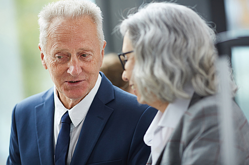 Serious wrinkled man in suit looking down and sharing business strategy with colleague